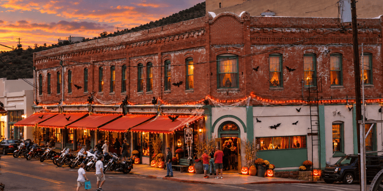 Historic brick mining-town building below a hillside, decorated for Halloween with jack-o'-lanterns and orange lights at dusk
