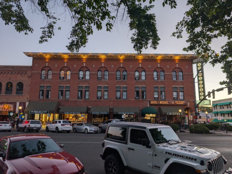 Hotel St. Michael at dusk with its lit roofline and vertical neon sign at the corner of Whiskey Row in Prescott, Arizona