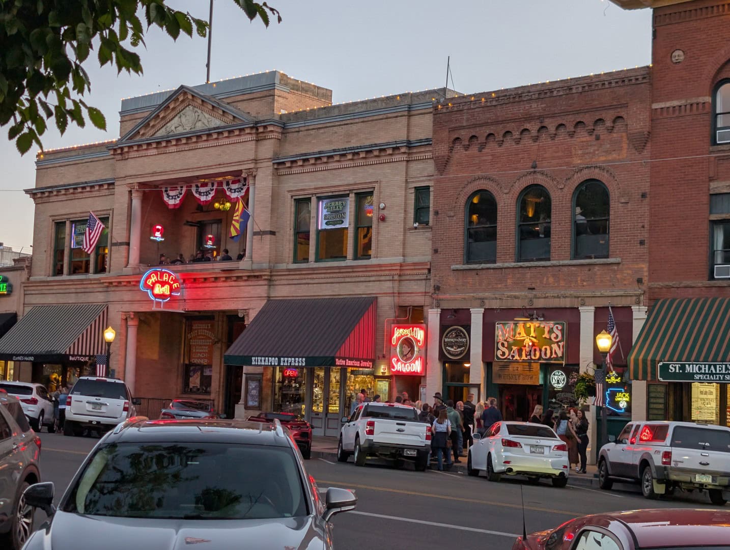 Whiskey Row at dusk with neon signs for the Palace, the Jersey Lilly, and Matt's Saloon and a crowd on the sidewalk in Prescott, Arizona