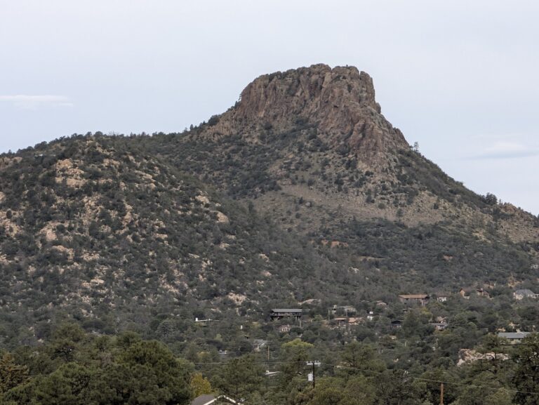 Thumb Butte's rocky volcanic summit rising above pine and juniper forest and hillside homes in Prescott, Arizona