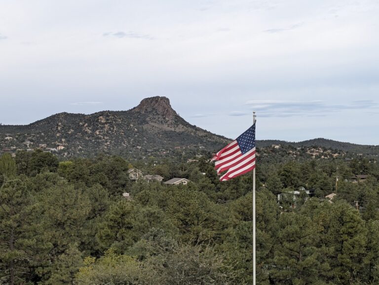 American flag waving over ponderosa pines with Thumb Butte on the skyline in Prescott, Arizona