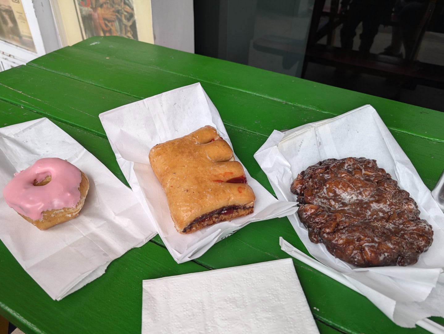 Pink frosted donut, raspberry-filled bear claw, and giant apple fritter on a green table at Outlaw Donuts in Prescott, Arizona